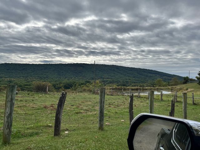 Fields and wooded hills beneath a cloudy sky.